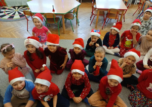 dzieci w czapkach mikołajkowych siedzą na wykładzinie