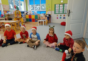 dzieci w czapkach mikołajkowych siedzą na wykładzinie