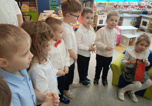 dzieci stoją w półkolu i składają życzenia jubilatce