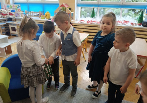 dzieci stoją w półkolu i składają życzenia jubilatce