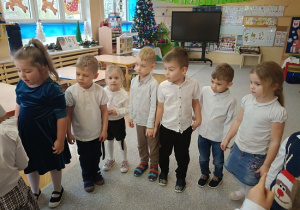 dzieci stoją w półkolu i składają życzenia jubilatce