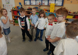 dzieci stoją w półkolu i składają życzenia jubilatce