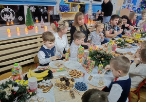 dzieci i rodzice siedzą przy stolikach i jedzą słodkości