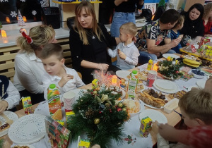 dzieci i rodzice siedzą przy stolikach i jedzą słodkości