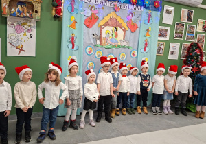 dzieci w czapkach mikołajkowych i strojach galowych prezentują wiersze i piosenki