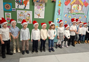 dzieci w czapkach mikołajkowych i strojach galowych prezentują wiersze i piosenki