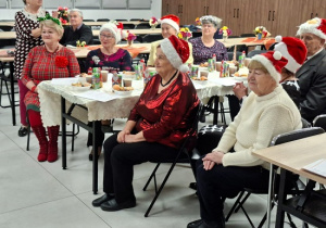 seniorzy w czapkach Mikołaja oglądają występy dzieci