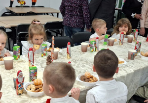 dzieci siedzą przy stołach jedzą słodycze i piją soki