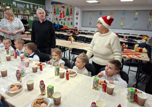 dzieci siedzą przy stołach jedzą słodycze i piją soki