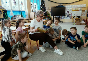 dzieci siedzą w półkolu i słuchają czytanej przez Panią książki
