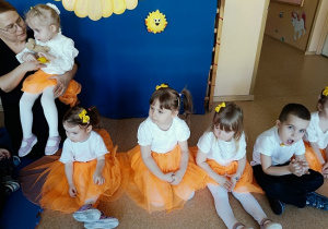 dzieci siedzą w pomarańczowych spódniczkach na podłodze