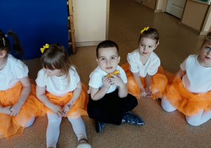 dzieci w odświętnych strojach siedzą na podłodze