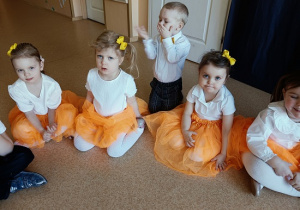 dzieci w odświętnych strojach siedzą na podłodze