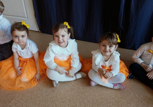 dzieci w odświętnych strojach siedzą na podłodze