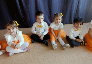 dzieci w odświętnych strojach siedzą na podłodze