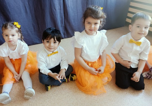 dzieci w odświętnych strojach siedzą na podłodze