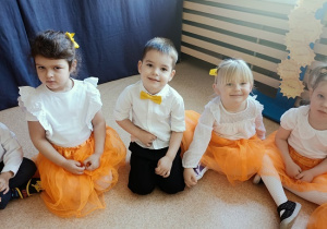 dzieci w odświętnych strojach siedzą na podłodze