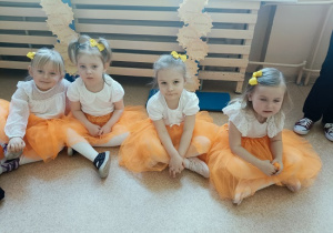 dzieci w odświętnych strojach siedzą na podłodze