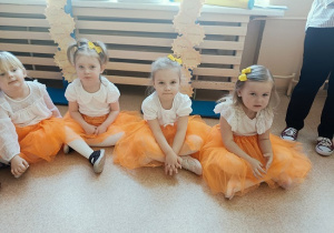 dzieci w odświętnych strojach siedzą na podłodze