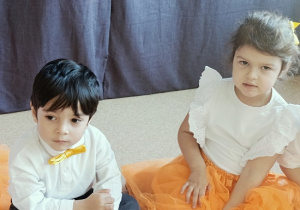 dzieci w odświętnych strojach siedzą na podłodze