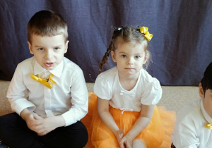 dzieci w odświętnych strojach siedzą na podłodze