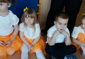 dzieci w odświętnych strojach siedzą na podłodze