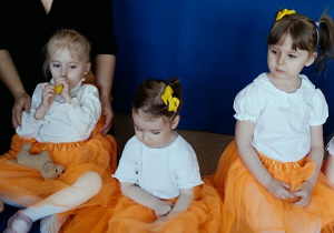 dzieci w odświętnych strojach siedzą na podłodze