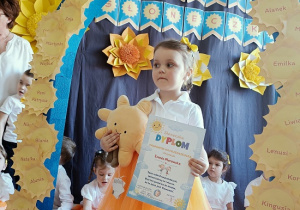 dziewczynka z dyplomem i maskotką pozuje do zdjęcia