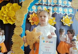 dziewczynka z dyplomem i maskotką pozuje do zdjęcia