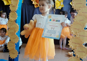 dziewczynka z dyplomem i maskotką pozuje do zdjęcia