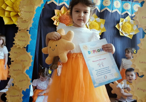 dziewczynka z dyplomem i maskotką pozuje do zdjęcia