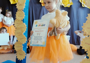 dziewczynka z dyplomem i maskotką pozuje do zdjęcia