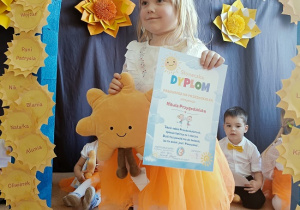 dziewczynka z dyplomem i maskotką pozuje do zdjęcia