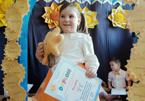 dziewczynka z dyplomem i maskotką pozuje do zdjęcia