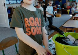 chłopiec sadzi cebulę do pojemniczka z ziemią