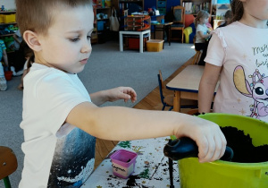 chłopiec sadzi cebulę do pojemniczka z ziemią