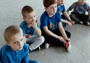 dzieci w niebieskich koszulkach siedzą na dywanie