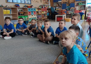 dzieci w niebieskich koszulkach siedzą na dywanie