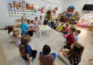dzieci i nauczycielka siedzą na dywanie i smakują pokrojone owoce