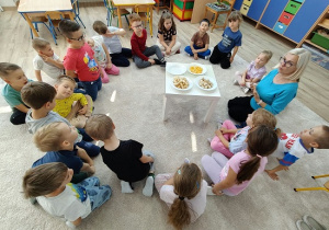 dzieci i nauczycielka siedzą na dywanie i smakują pokrojone owoce
