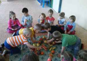 dzieci ogladają na dywanie owoce i warzywa
