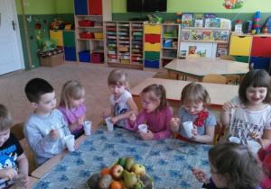 dzieci przy stolikach zajadają musy owocowe