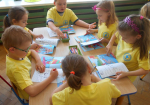 Dzieci przy niebieskim stoliku kolorują w książce