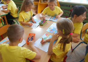 Dzieci przy czerwonym stoliku kolorują w książce
