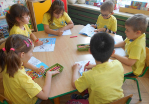 Dzieci przy zielonym stoliku kolorują w książce