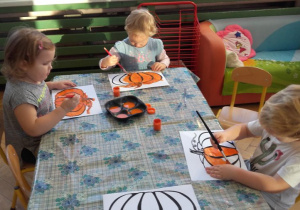 Maja, Hania i Wojtuś malują farbami kolorowankę dyni