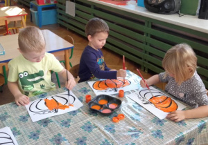 Ola, Kamil i Adaś malują farbami kolorowankę dyni