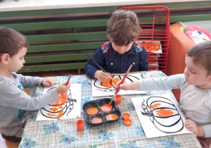 Mikołaj, Krzyś i Emil malują farbami kolorowankę dyni