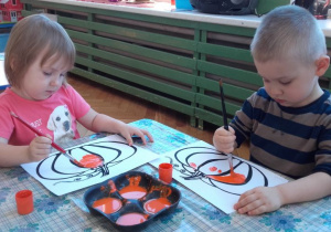 Michalinka i Dominik malują farbami kolorowankę dyni