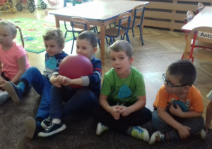 dzieci siedzą w gromadce i uważnie słuchają